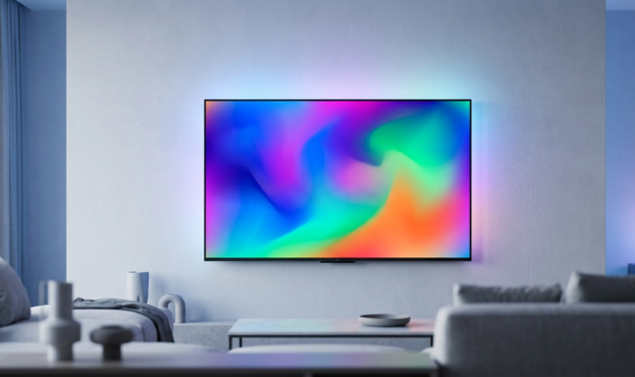 A modern flatscreen television mounted on a living room wall, displaying a colorful abstract picture on screen with soft blue ambient lighting.